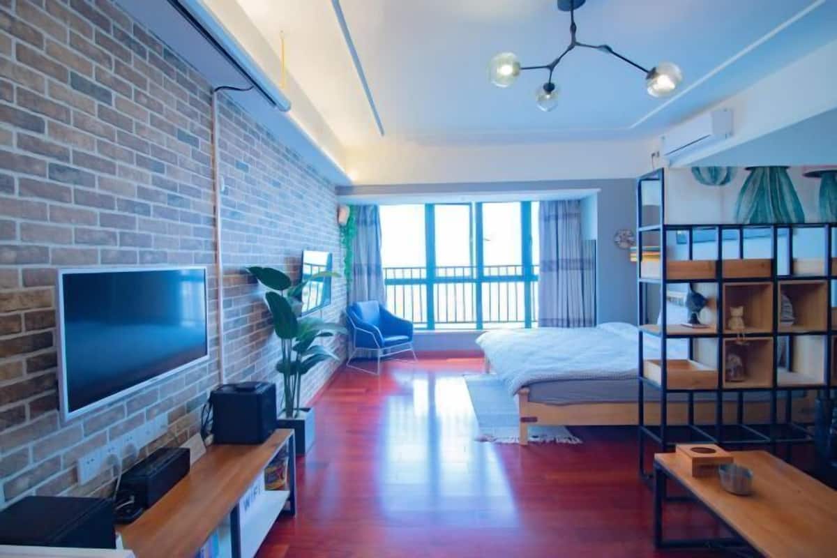 Une chambre d’hôtel moderne avec un mur en briques, un téléviseur à écran plat, un lit, un bureau, une chaise et une grande fenêtre donnant sur un paysage agréable.