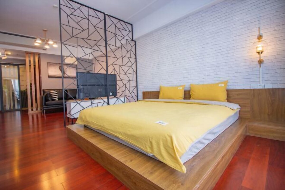 Un dormitorio moderno con una cama plataforma de madera, un separador geométrico y una pared de ladrillo blanco.