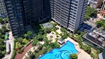 A high-rise building with a rooftop pool surrounded by greenery and a small garden area.
