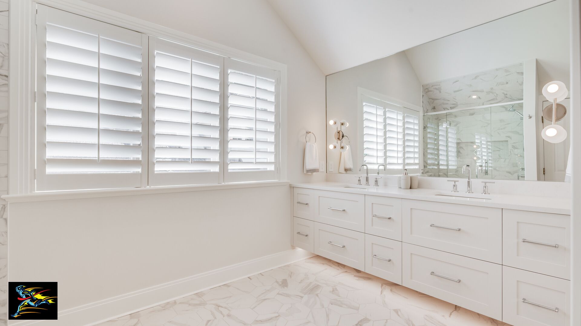 A bathroom with white cabinetry, a large mirror with lights, and a window with blinds.