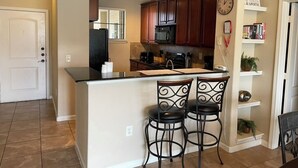 Una cocina con una isla central, taburetes de bar, armarios de madera y un reloj en la pared.