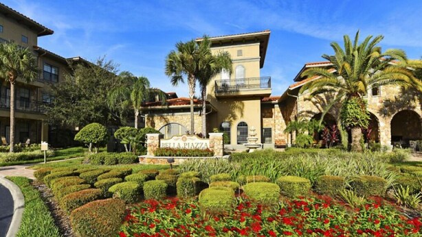 Un hotel con un letrero que dice "Bella Piazza", rodeado de jardines cuidados y palmeras.
