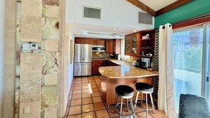 A kitchen with a central island, bar stools, and a view through the glass door. - Walk Downtown, 2 Large Mountain View Patios (Palm Springs)