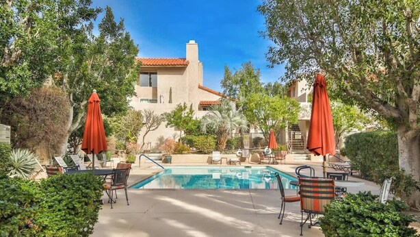 A pool area with lounge chairs and umbrellas, surrounded by greenery and a building with a red-tiled roof. - Walk Downtown, 2 Large Mountain View Patios (Palm Springs)