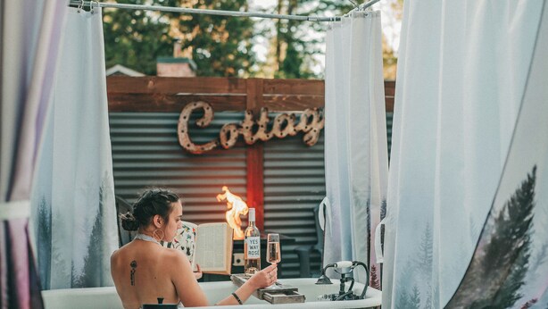 A bathtub with a towel hanging over it, a bottle of lotion, and a candle on a table. - Forest Cottage with Hot Tub, Outdoor Baths & Alpacas (Grants Pass)