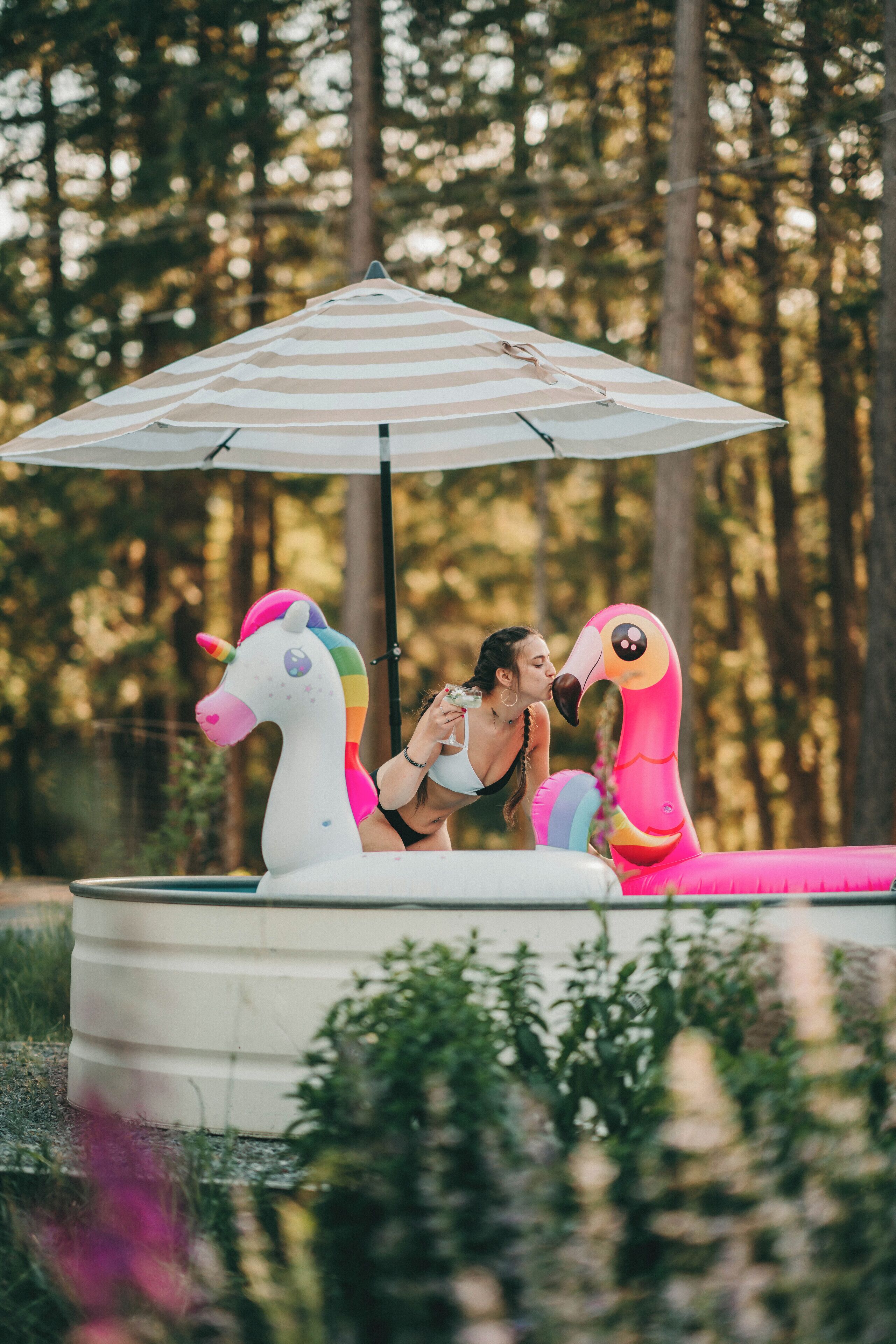 Una piscina con gonfiabili a forma di unicorno e fenicottero, circondata da vegetazione.