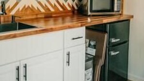 A kitchen with wooden shelves, a microwave, and white cabinets. - Forest Cottage with Hot Tub, Outdoor Baths & Alpacas (Grants Pass)