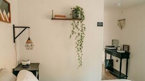 A bedroom with a bed, a bedside table with a lamp, a shelf with a plant, and a desk with a computer. - Forest Cottage with Hot Tub, Outdoor Baths & Alpacas (Grants Pass)