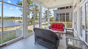 A covered porch with large windows, a ceiling fan, a red sofa, and wicker furniture.