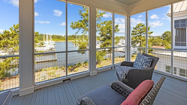 A covered outdoor area with a view of boats on a lake, wicker furniture, and a railing.