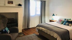 A bedroom with a bed, a nightstand, a lamp, a fireplace, and a window with curtains.