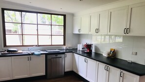 A kitchen with white cabinets, a stainless steel dishwasher, and a window with a view of trees.