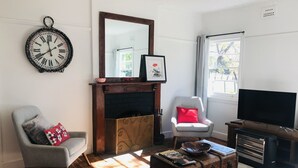 A living room with a fireplace, a clock, a television, a chair, a sofa, and a wooden chest.