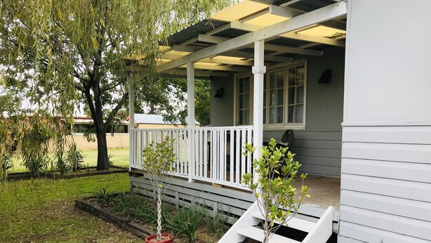 A covered porch with a white railing, potted plants, and a brick pathway leading to a house with a gray exterior.