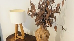A wooden table with a wicker vase containing dried leaves and a white lamp with a wooden base.