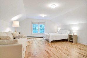Een kamer met een bed, een bank, een raam en een radiator.