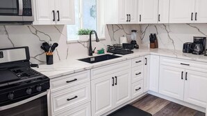 A modern kitchen with white cabinets, a black stove, a sink, and a window with a view. - Newly built guest house with full kitchen and washer/dryer (Simi Valley)