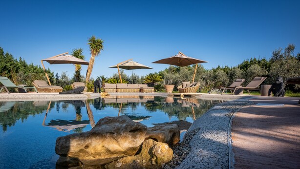 A pool area with lounge chairs, umbrellas, and a rock feature. - Relais San Baio (Cecina)