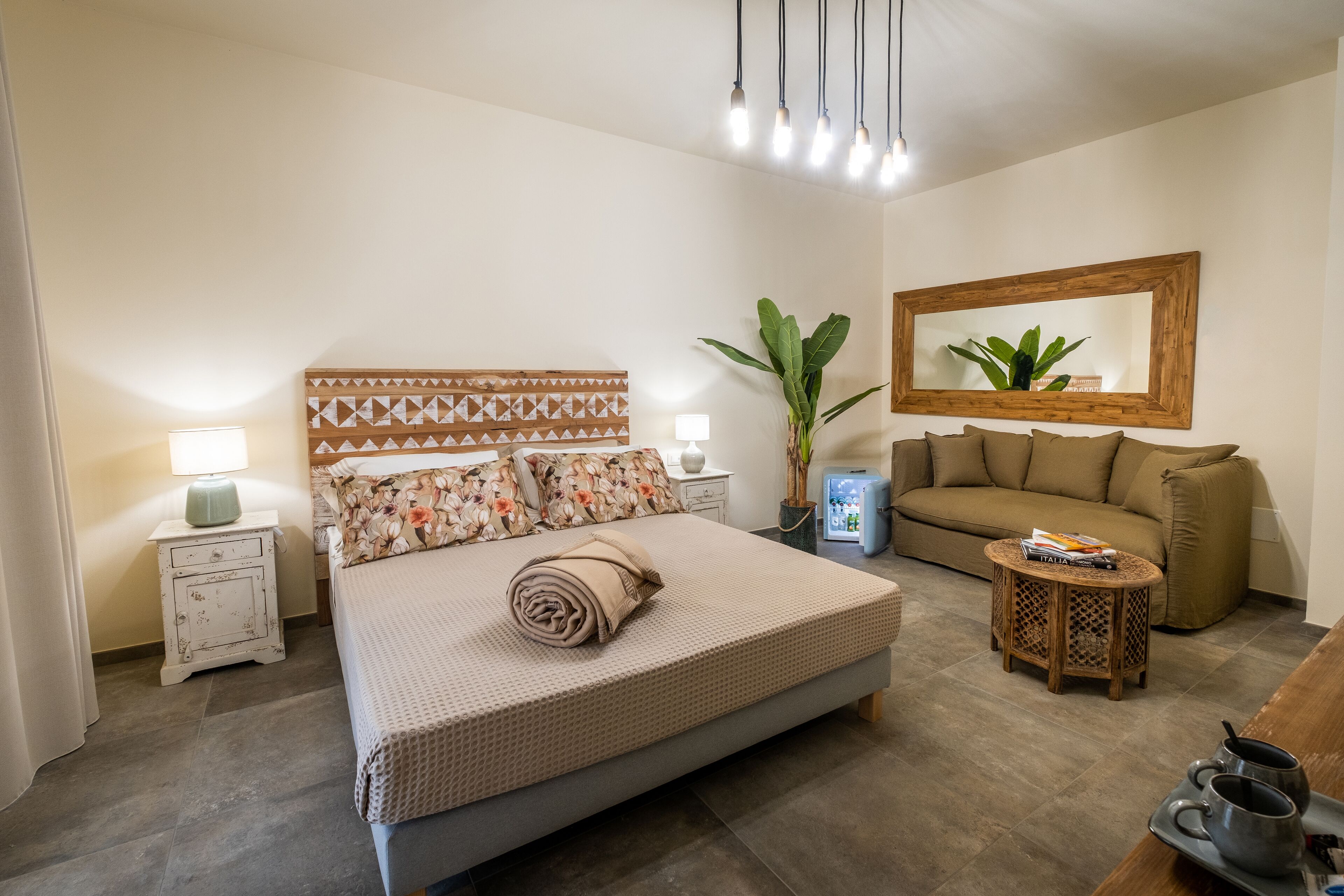 A bedroom with a large bed, a sofa, a small table, and a mirror.