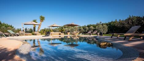 Uma área de piscina com espreguiçadeiras, guarda-sóis e um céu azul límpido.