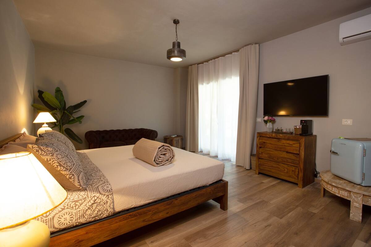 A bedroom with a bed, bedside lamp, dresser, TV, and a plant.