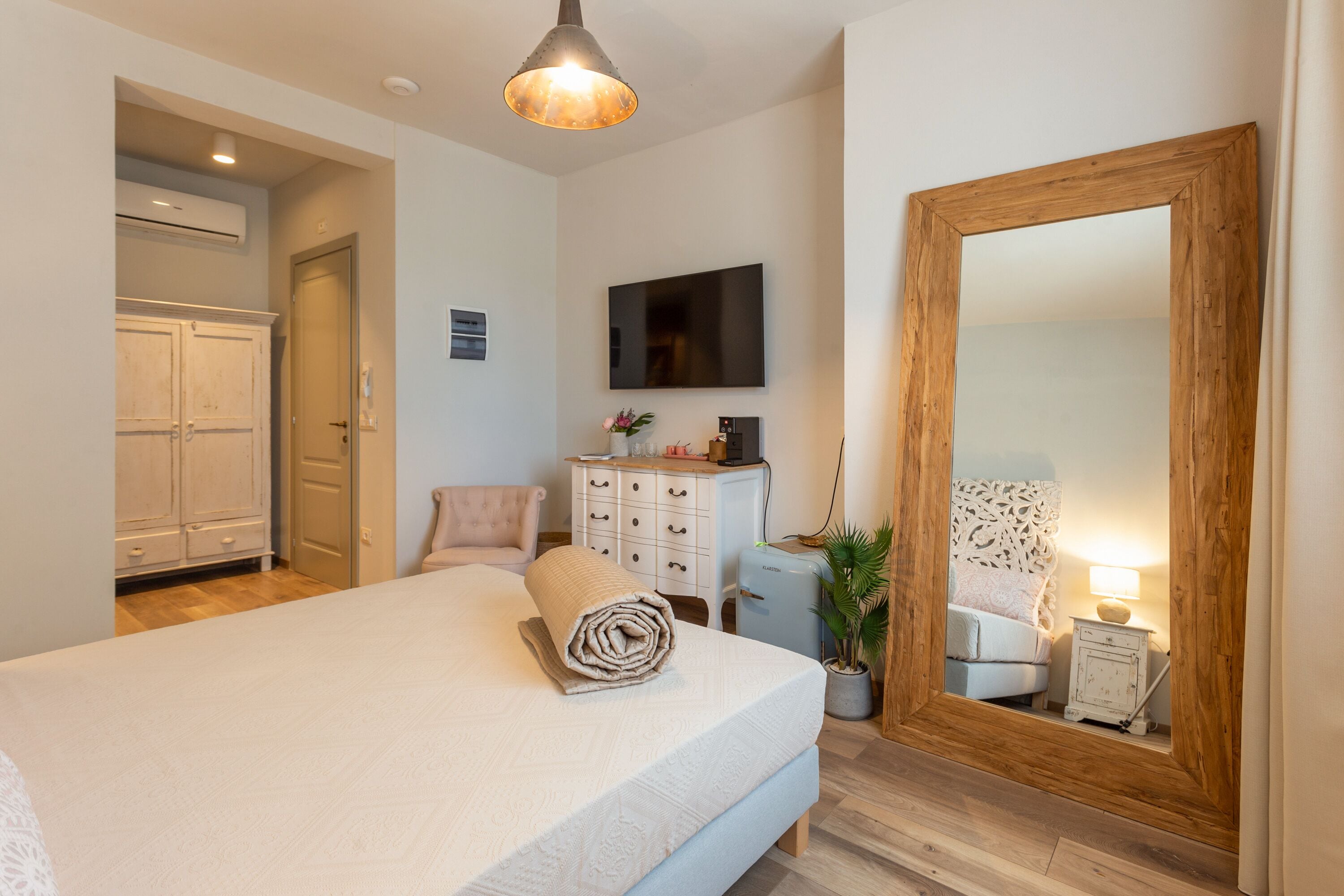 A bedroom with a bed, a dresser, a TV, a mirror, and a potted plant.