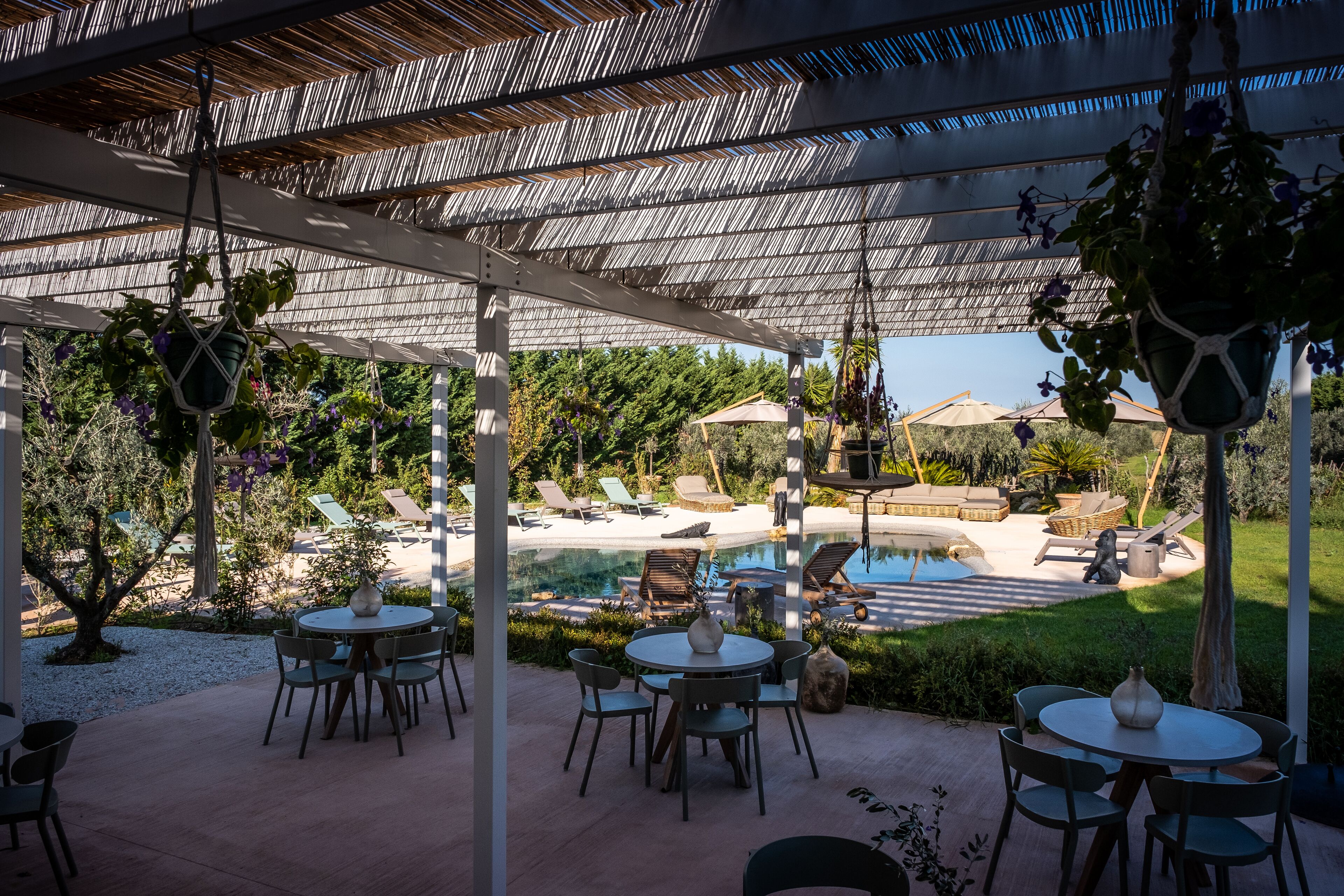 An outdoor patio with round tables and chairs, a pool, and lounge chairs.