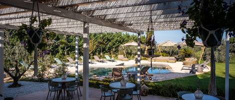 An outdoor patio with round tables and chairs, a pool, and lounge chairs.