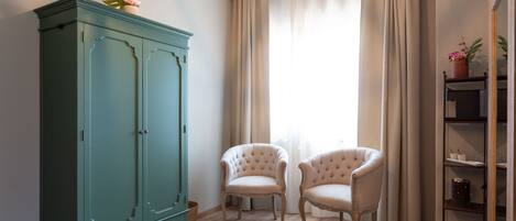 A room with a green wardrobe, two upholstered chairs, a wooden floor, and a window with curtains.