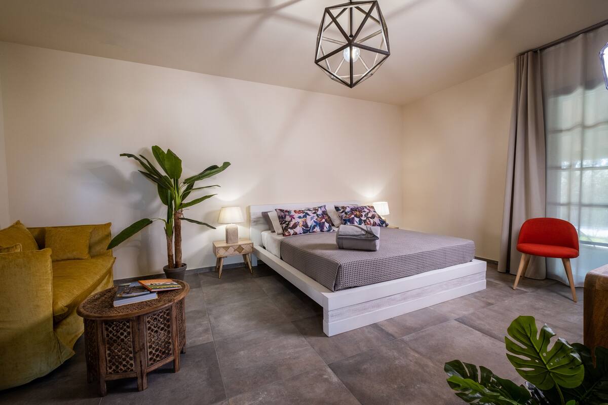 A modern bedroom with a bed, a sofa, a small table, a potted plant, and a red chair.