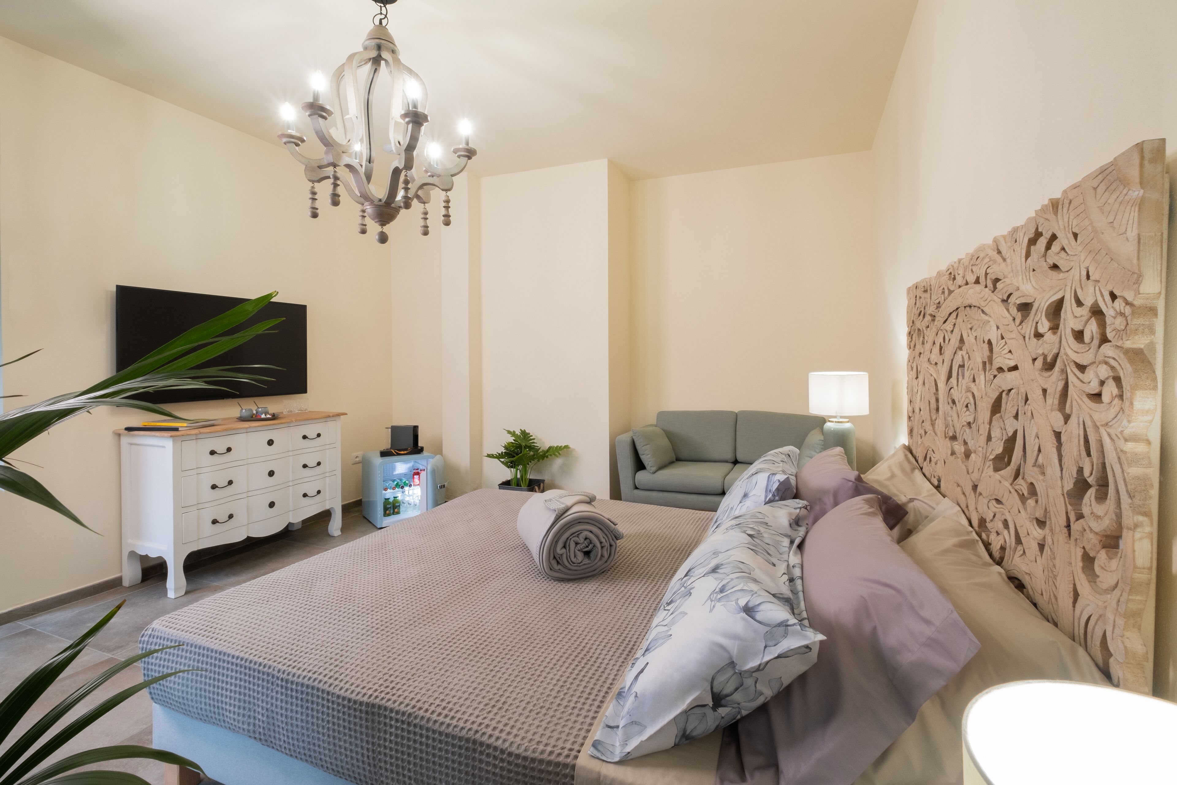 Quarto com cama, televisão, cômoda, candelabro e cabeceira decorativa.