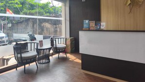 A reception area with a wooden reception desk, two chairs, a window with a view of the street, and a wall-mounted decorative element. - Collection O near Lampung City Mall formerly Royal Guesthouse (Bandar Lampung)