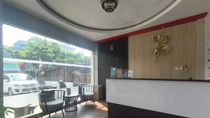 A reception area with a wooden reception desk, a wall-mounted decorative piece, and a view of the street outside. - Collection O near Lampung City Mall formerly Royal Guesthouse (Bandar Lampung)