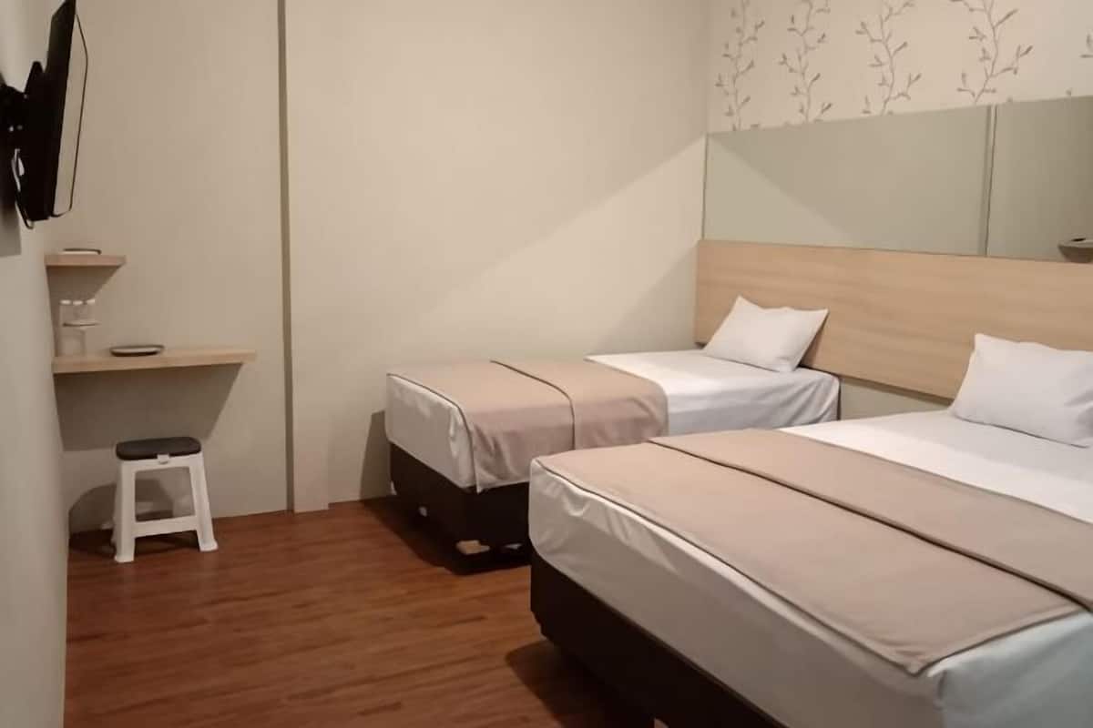 Habitación de hotel con dos camas, un taburete pequeño, piso de madera y un estante en la pared.