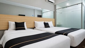 Een hotelkamer met twee bedden, een houten hoofdeinde, een glazen scheidingswand en een airconditioner.