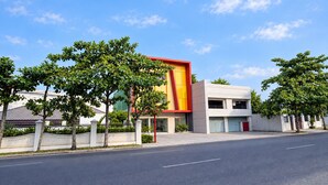 Een modern gebouw met een opvallende rode en gele gevel, omgeven door bomen en een heldere lucht.