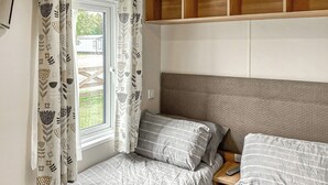Een slaapkamer met twee bedden, een raam met gordijnen en een houten hoofdeinde.