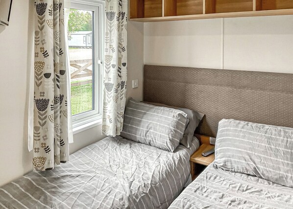 A bedroom with two beds, a window with curtains, and a wooden headboard.