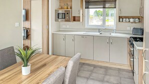Une cuisine moderne avec une table à manger en bois, des chaises grises, une plante en pot et une fenêtre avec des stores.