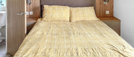 Una cama con colcha estampada, cabecera de madera, lámparas de noche y un armario de madera.
