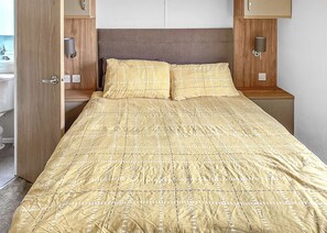 Ein Bett mit gemustertem Überwurf, einem Holz-Kopfstück, Nachttischlampen und einem Holzschrank.