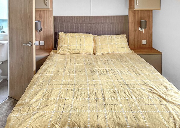 A bed with a patterned bedspread, a wooden headboard, bedside lamps, and a wooden wardrobe.