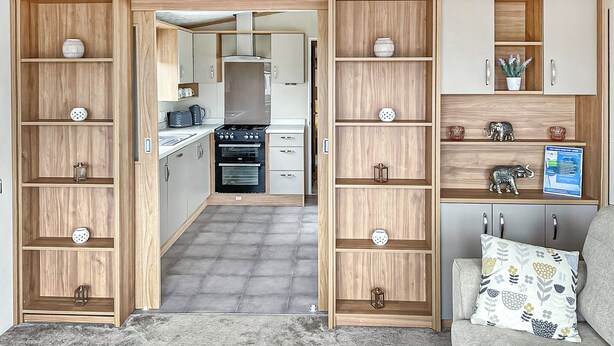 Un espace de vie compact comprenant un coin cuisine, des étagères en bois et un canapé agrémenté de coussins à motifs.