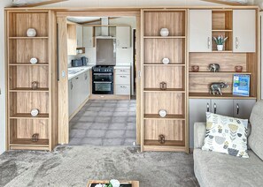 A compact living space with a kitchenette, wooden shelving, and a sofa with patterned cushions.