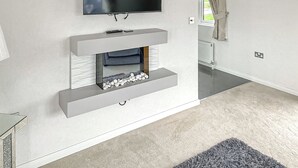 A modern living room with a flat-screen TV mounted on the wall, a built-in fireplace with a stone surround, and a grey carpet.