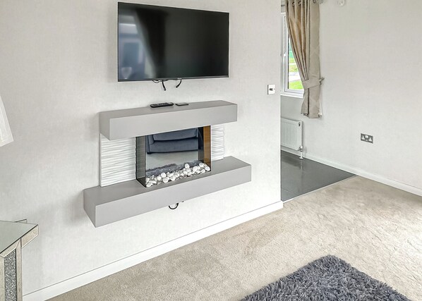 A modern living room with a flat-screen TV mounted on the wall, a built-in fireplace with a stone surround, and a grey carpet.