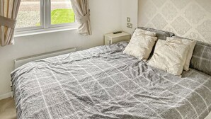 A bedroom with a bed, a nightstand, a window with curtains, and a radiator. - 2 bedroom accommodation in Laurenkirk (Laurenkirk)
