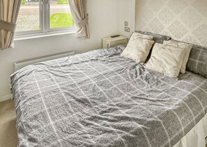Een slaapkamer met een bed, nachtkastje, raam met gordijnen en een radiator.