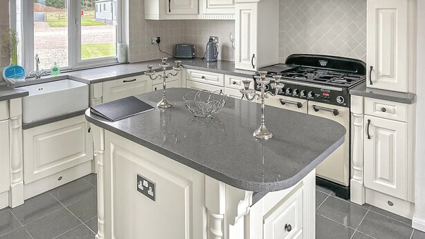A kitchen with a large island, white cabinetry, a stove, and a view of the outdoors.