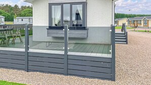 A single-story mobile home with a balcony, a gravel driveway, and a clear sky.